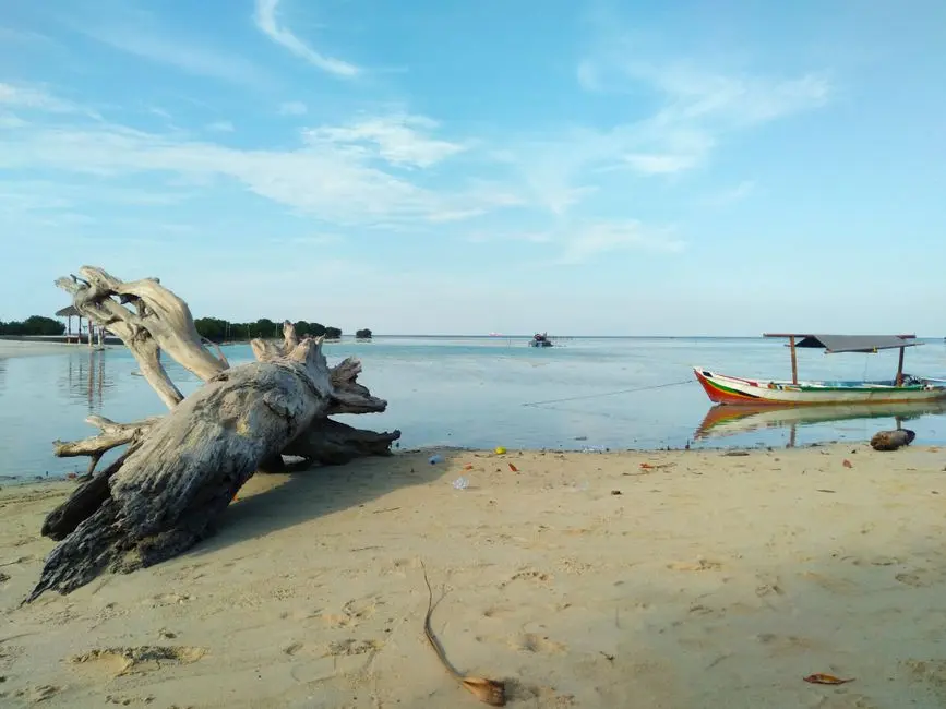 Pemandangan pantai pasir putih di Tiakur dengan air jernih dan perahu nelayan